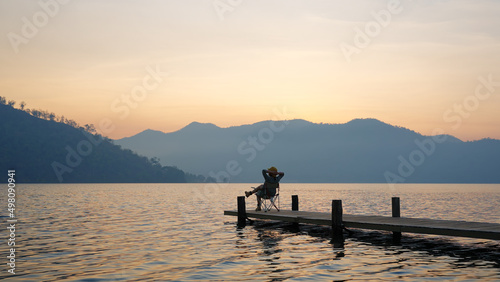 Asia people woman enjoy sit calm day dream on cozy chair at river pier hand behind head. Wide view of cloud dawn dusk sky solo budget staycation getaway at glamping take city life break stress relief. © ChayTee