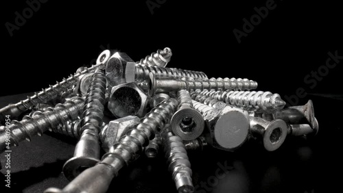 Pile of steel chrome screws rotating on isolated black background. Stainless steel bolts, metal anchor bolts on the table. Metallic helical carving joinery. Macro close up. Slow motion ready 59.97fps. photo