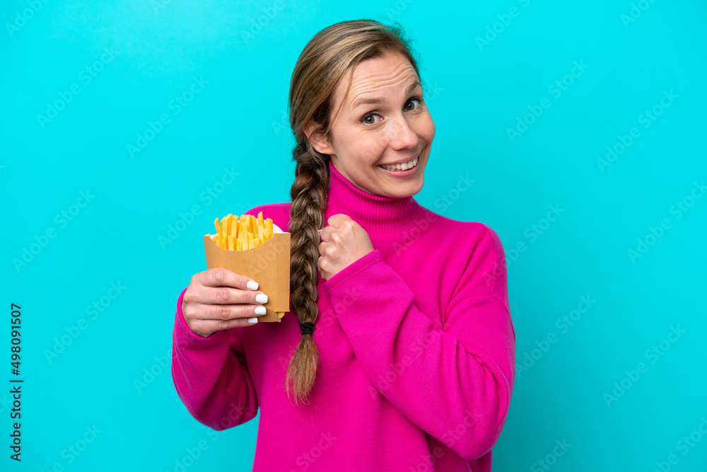 Young caucasian woman holding fried chips isolated on blue background celebrating a victory Young caucasian woman holding fried chips isolated on blue background celebrating a victory