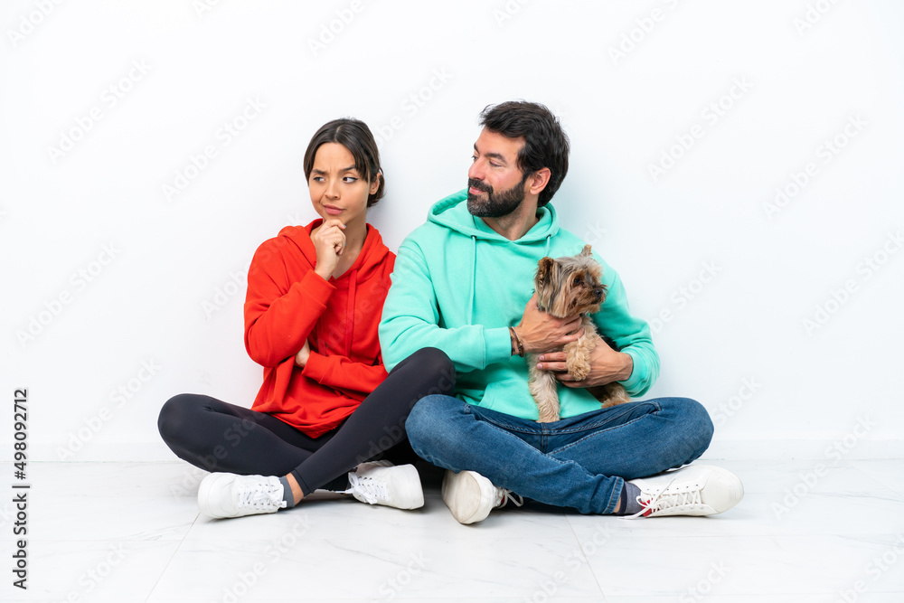 Young caucasian couple sitting on the floor with their pet isolated on white background looking to the side Young caucasian couple sitting on the floor with their pet isolated on white background looking to the side
