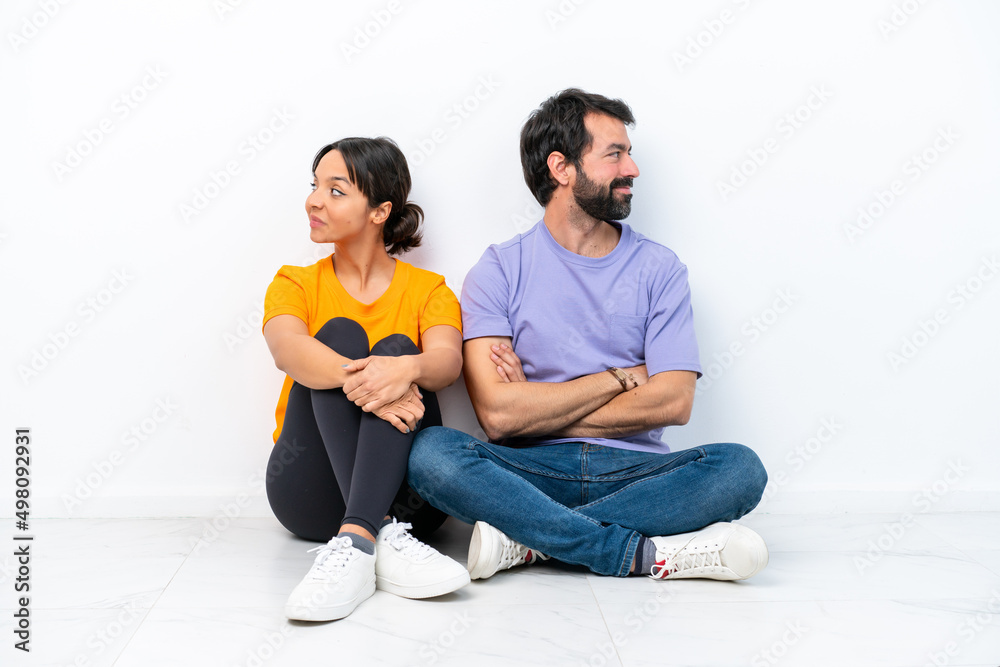 Young caucasian couple sitting on the floor isolated on white background keeping arms crossed Young caucasian couple sitting on the floor isolated on white background keeping arms crossed