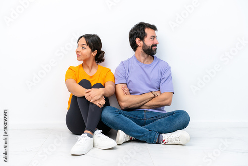 Young caucasian couple sitting on the floor isolated on white background keeping arms crossed