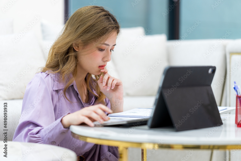 Young Asian woman sitting on the living room floor calculates monthly expenses using calculator check utility bills managing family budget, accountant do paperwork job at home concept. Young Asian woman sitting on the living room floor calculates monthly expenses using calculator check utility bills managing family budget, accountant do paperwork job at home concept.