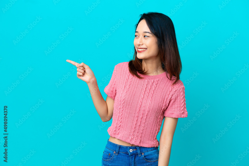 Young Vietnamese woman isolated on blue background pointing finger to the side and presenting a product Young Vietnamese woman isolated on blue background pointing finger to the side and presenting a product