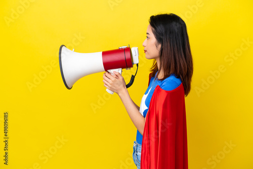 Super hero Vietnamese woman isolated on yellow background shouting through a megaphone