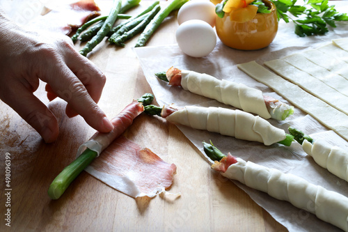 Preparazione degli asparagi avvolti nel prosciutto e nella pasta sfoglia sulla tavola di legno. Sfizioso antipasto primaverile. Direttamente sopra. photo
