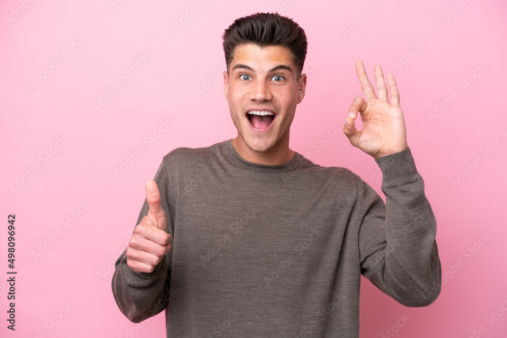 Young caucasian man isolated on pink background showing ok sign and thumb up gesture Young caucasian man isolated on pink background showing ok sign and thumb up gesture