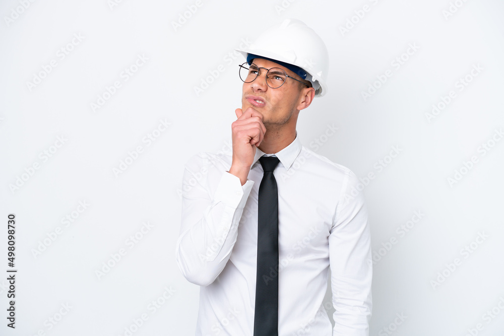 Young architect caucasian man with helmet and holding blueprints isolated on white background having doubts