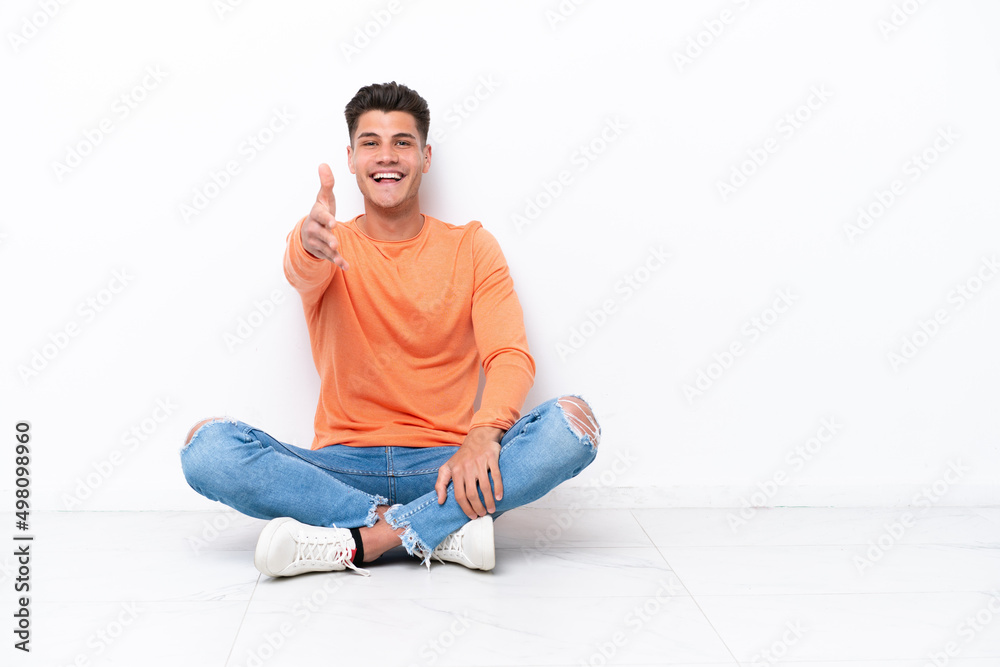 Young man sitting on the floor isolated on white background shaking hands for closing a good deal Young man sitting on the floor isolated on white background shaking hands for closing a good deal