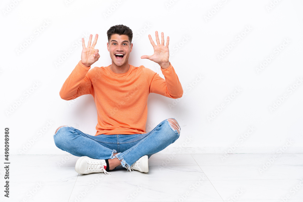 Young man sitting on the floor isolated on white background counting eight with fingers