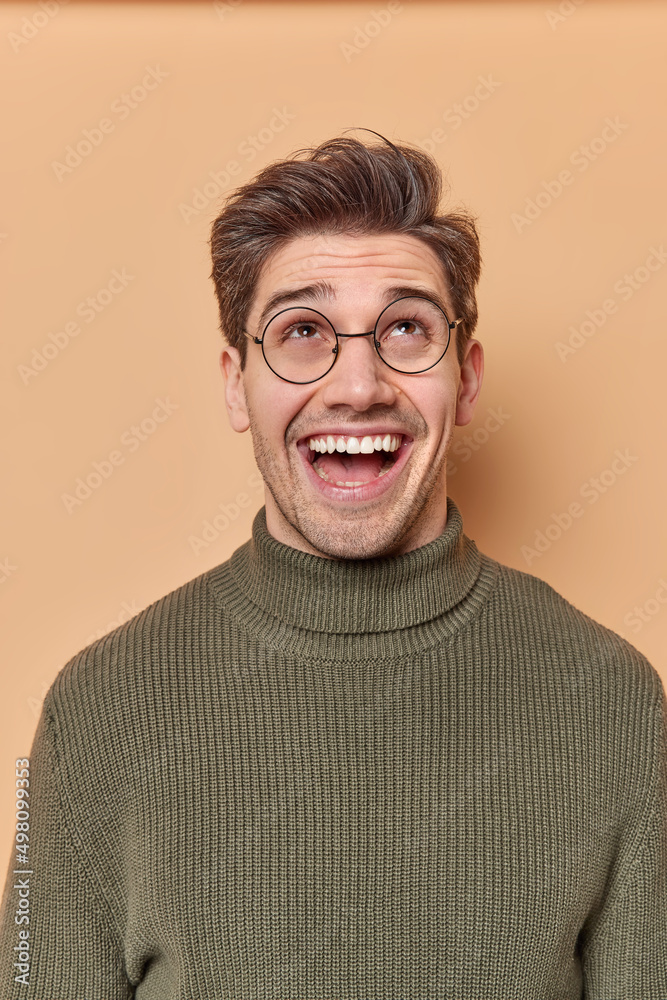 Vertical shot of handsome cheerful European man focused above on ceiling laughs positively sees something funny overhead dressed in casual jumper isolated over brown background. Wow what great offer Vertical shot of handsome cheerful European man focused above on ceiling laughs positively sees something funny overhead dressed in casual jumper isolated over brown background. Wow what great offer