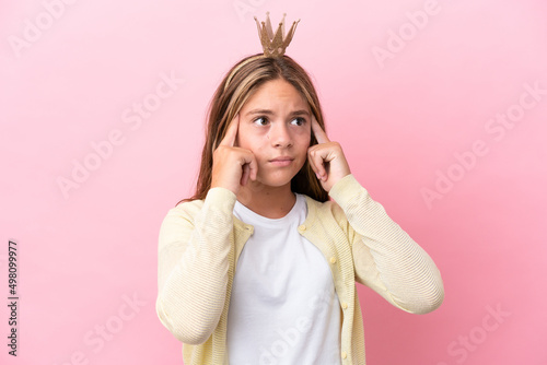 Little princess with crown isolated on pink background having doubts and thinking