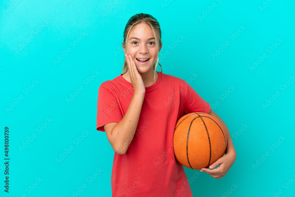 Little caucasian girl playing basketball isolated on blue background with surprise and shocked facial expression