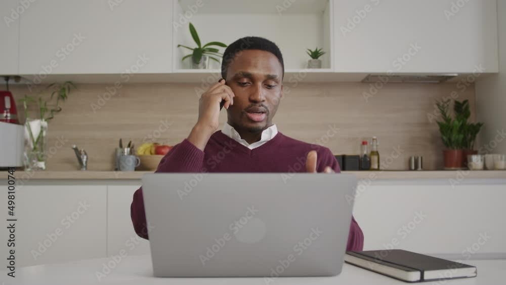 Young adult businessman having a call on his phone in front of his laptop Young adult businessman having a call on his phone in front of his laptop