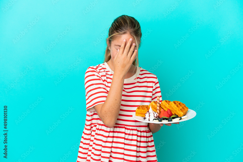 Little caucasian girl holding waffles isolated on blue background laughing