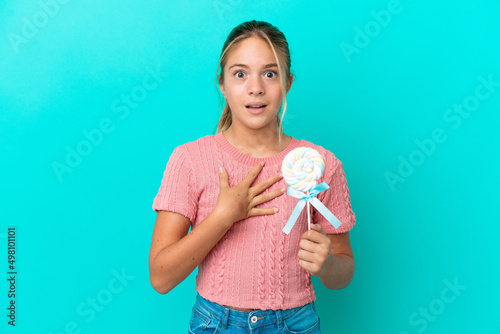 Little Caucasian girl holding a lollipop isolated on blue background surprised and shocked while looking right
