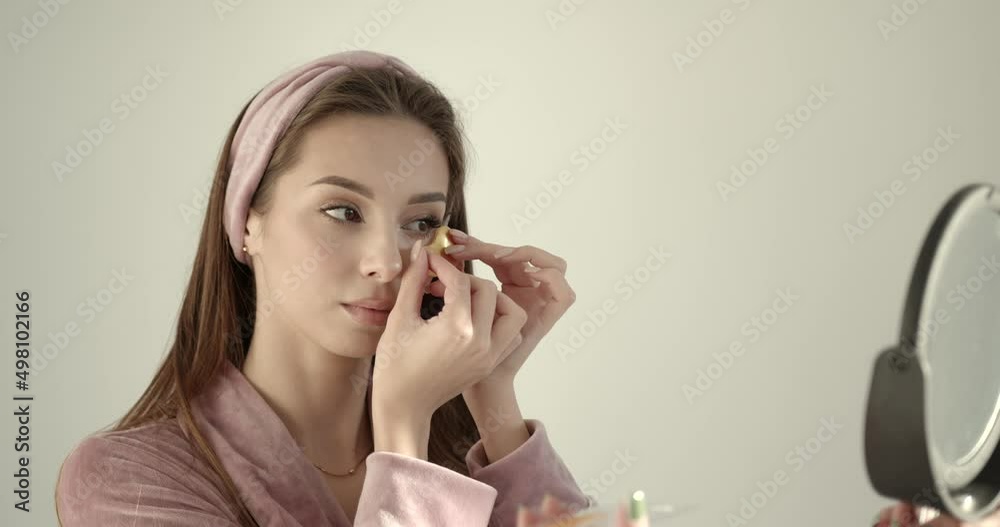 Woman applying hydrogel under-eye recovery patches on a light background Woman applying hydrogel under-eye recovery patches on a light background