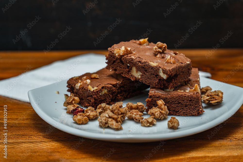 Homemade chocolate brownie squares with pecan pieces served on a white plate. Natural, healthy food concept. Homemade chocolate brownie squares with pecan pieces served on a white plate. Natural, healthy food concept.