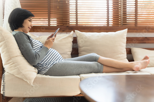 Happy Asian pregnant woman sitting on sofa using digital tablet at home, Online Shopping