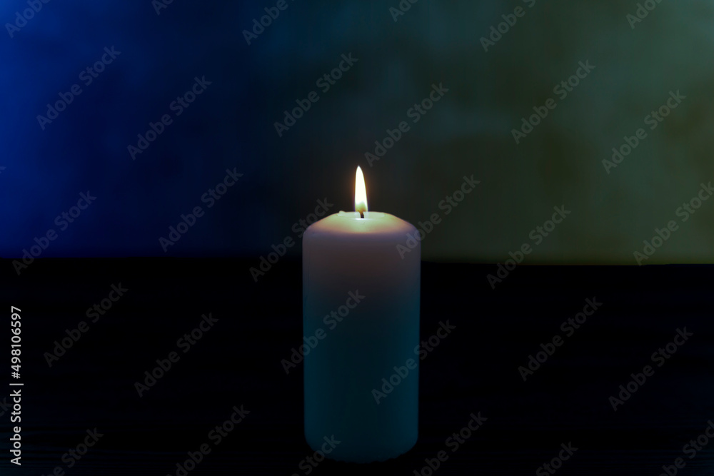 Biała świeca płonąca na ciemnym tle posiadającym delikatne niebieski i żółte zabarwienie. Hołd i wyraz solidarności z ofiarami wojny w Ukrainie. - obrazy, fototapety, plakaty 