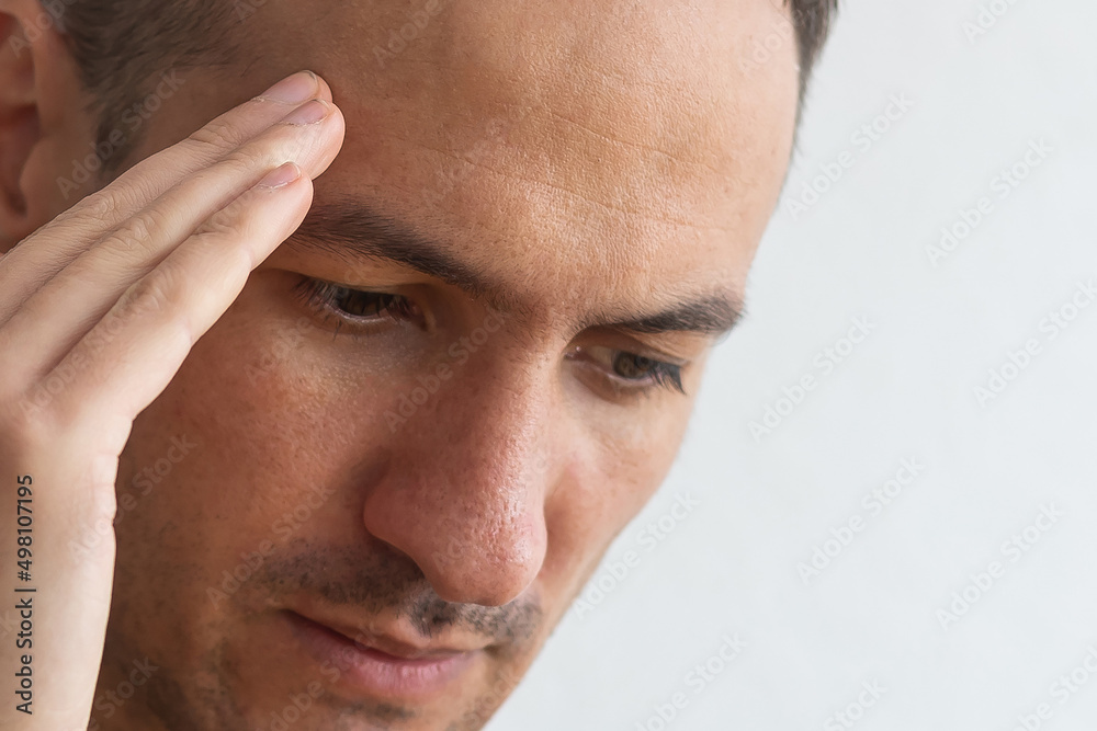 Obraz premium Horizontal photo of good-looking Caucasian man pictured isolated on gray background in right side of picture showing how much his head hurts, experiencing pain, looking miserable and exhausted