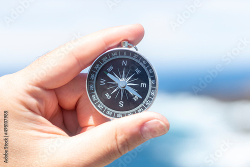 Closeup, hand holding an analog compass in front of the sea, summer concept, holidays, travelling. Selective focus.