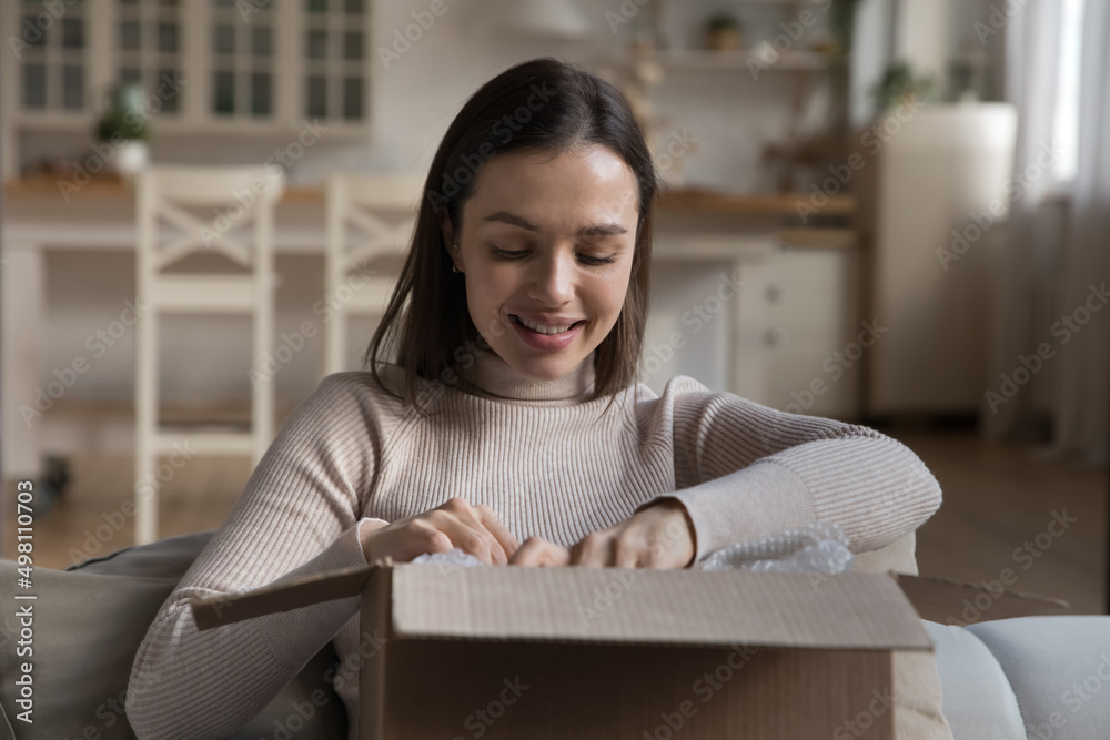 Happy young customer woman receiving purchase from internet store, unpacking parcel, opening cardboard box, package, holding paper container, smiling. Delivery, transportation, postal service Happy young customer woman receiving purchase from internet store, unpacking parcel, opening cardboard box, package, holding paper container, smiling. Delivery, transportation, postal service