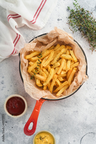 French fries. Tasty French fries server in red cast iron skillet with tomato and cheese sauce on old gray concretetable background. Diverse Keto Dishes. Fast food and unhealthy food concept. photo