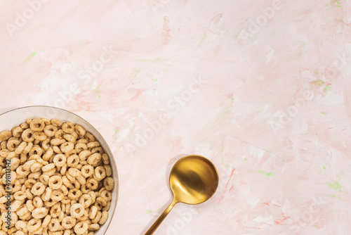 Delicious honey cheerios cereal in a bowl and golden spoon on pink background. Top view, flat lay, copy space. Breakfast concept photo