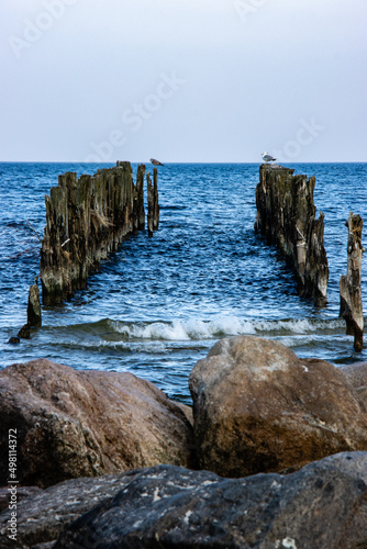 Old wooden poles on the shores of the Baltic Sea with stones in the foreground
