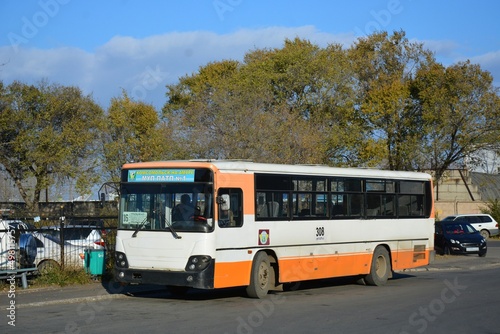 The bus is white and orange on the background of trees