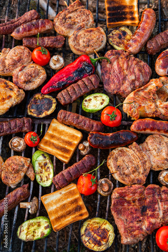 A large variety of grilled meat on the fire outside. Picnic with meat: sausages, pork steak, chicken breast with vegetables. 