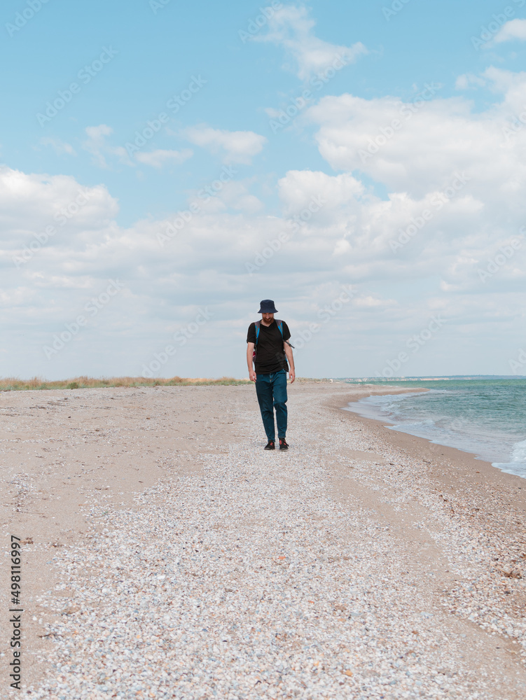 Smiling bearded millennial man in bucket hat black t-shirt walking on empty beach. Authentic male tourist lifestyle photo. Hipster guy outdoor. Solo travel adventure concept Active walking backpacking Smiling bearded millennial man in bucket hat black t-shirt walking on empty beach. Authentic male tourist lifestyle photo. Hipster guy outdoor. Solo travel adventure concept Active walking backpacking