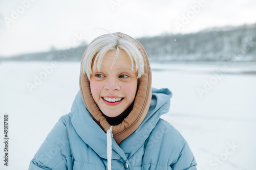 Positive woman with white hair walks in nature in winter during a snowfall against the backdrop of snowy views, looks away and smiles.