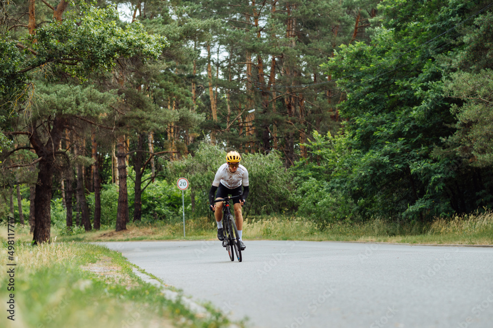 Male professional cyclist rides a bike out of town in the park on an asphalt country road in the woods