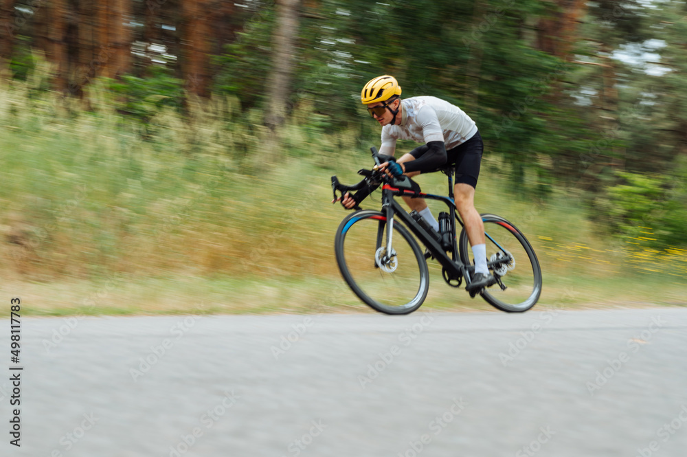 A professional cyclist in sportswear rides quickly on a country road. A professional cyclist in sportswear rides quickly on a country road.
