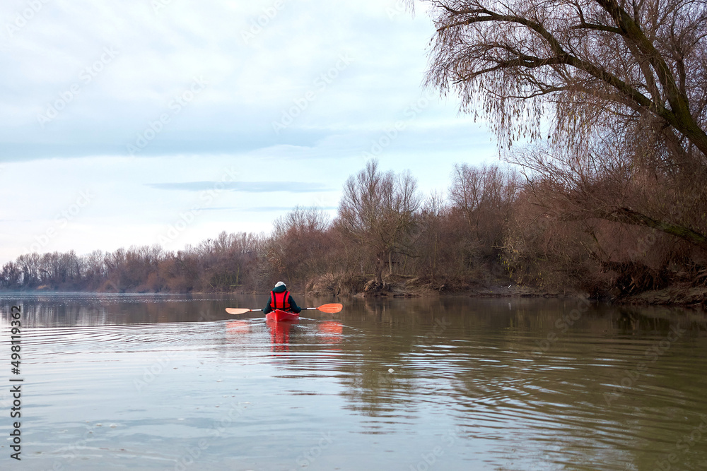 Woman in the red kayak rowing on the river on a cloudy calm winter day on the Danube River. Winter kayaking.