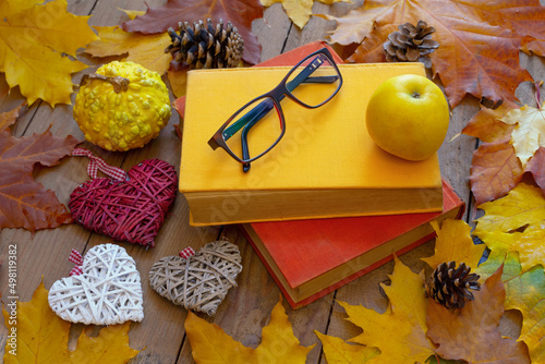 Autumn background. Old books, apple, glasses and decorative hearts on wooden planks with autumn leaves. Autumn design concept.