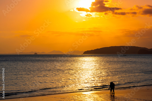 Relaxing sea sunset and romantic couple silhouettes walking on the beach in golden sunlight.