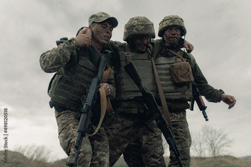 Fototapeta premium Two Ukrainian soldiers drag wounded warrior after battle against russian enemy.
