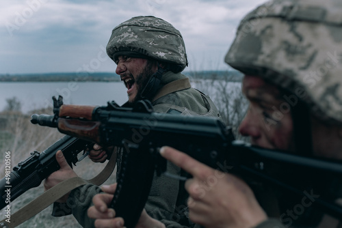 Tableau sur toile Two Ukrainian soldiers scream in rage and shoot from kalashnikov assault rifles to russian enemy