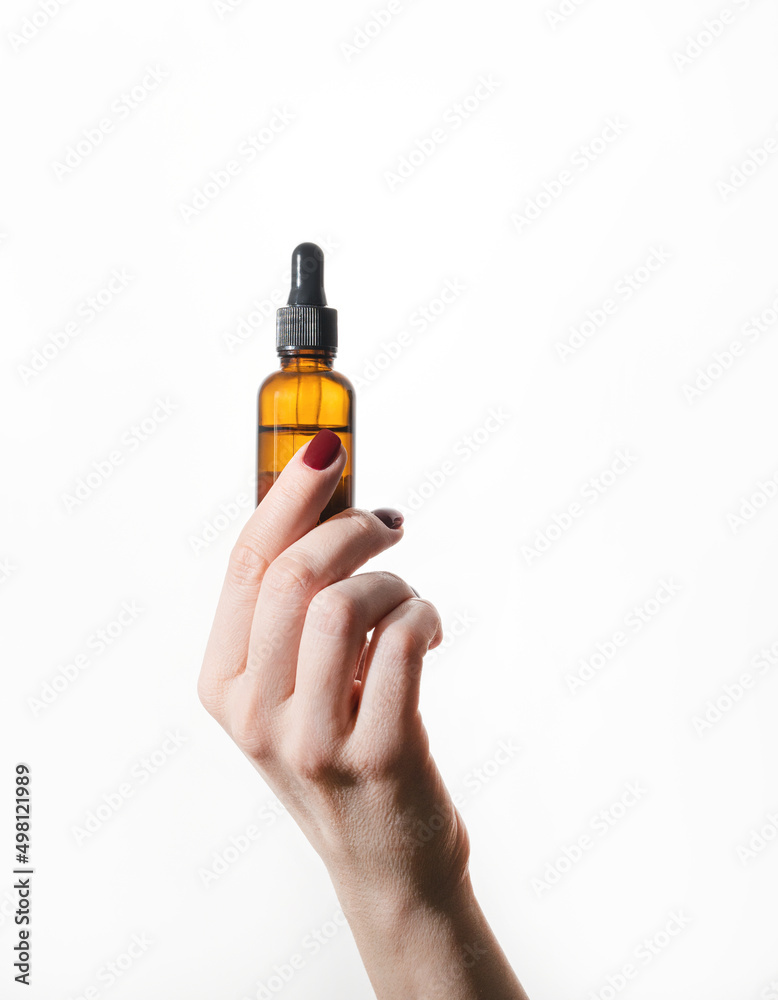 A woman's hand holds a bottle of cosmetics with serum for face and body on a white background. Skin care, beauty, body treatment concept. Copy space A woman's hand holds a bottle of cosmetics with serum for face and body on a white background. Skin care, beauty, body treatment concept. Copy space