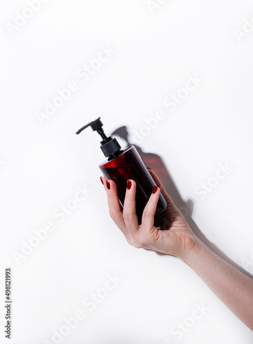A woman's hand holds a bottle of cosmetics with soap, sanitizer, creme or lotion for face and body on a white background with hard shadow. Skin care, beauty, body treatment concept. Copy space