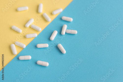 White pills on a yellow and blue pastel background. Capsules pills close-up. health care and medicine.