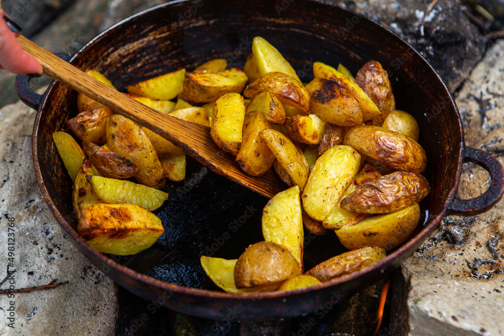 Homemade crispy potatoes on a frying pan on the fire outside. Picnic in nature with cooking. Homemade crispy potatoes on a frying pan on the fire outside. Picnic in nature with cooking.