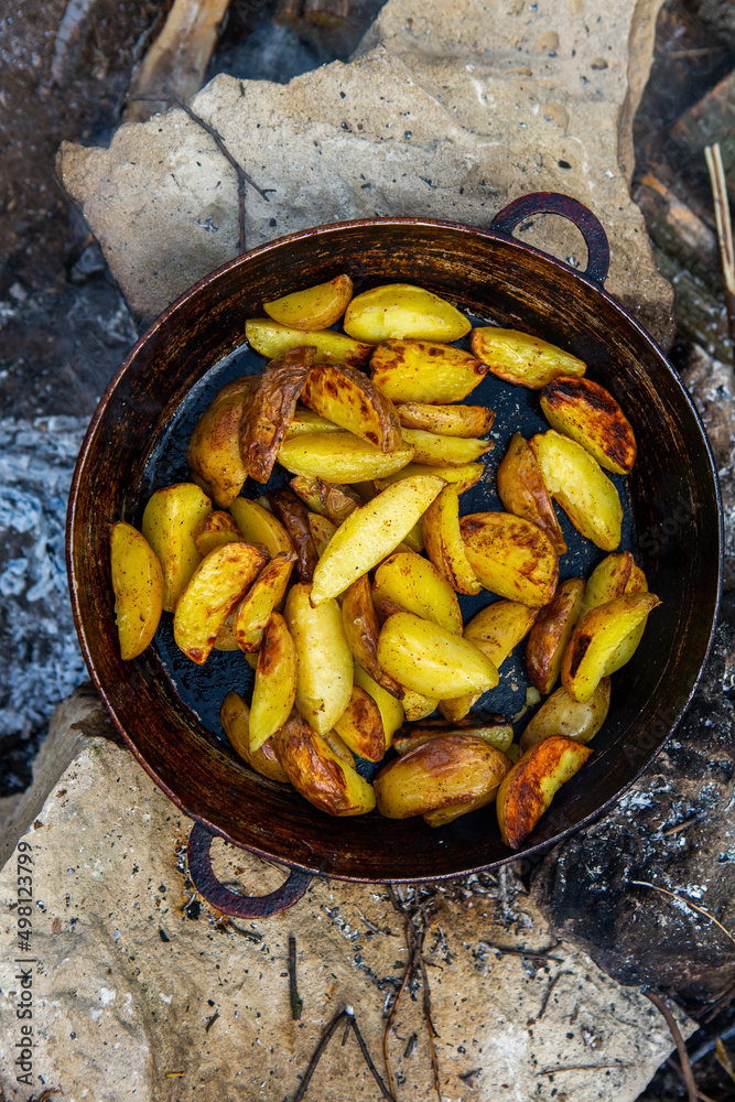Homemade crispy potatoes on a frying pan on the fire outside. Picnic in nature with cooking. Homemade crispy potatoes on a frying pan on the fire outside. Picnic in nature with cooking.
