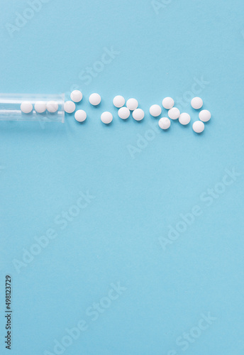 Different white pills and a plastic container on a blue background. Medical theme.