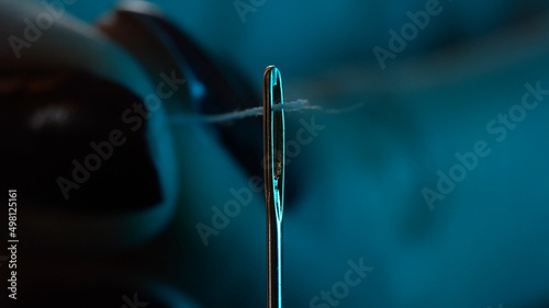 a woman's tailor hand insert With  sewing thread in a needle hole. fabric cloth concept, needlework, craft object © Ser