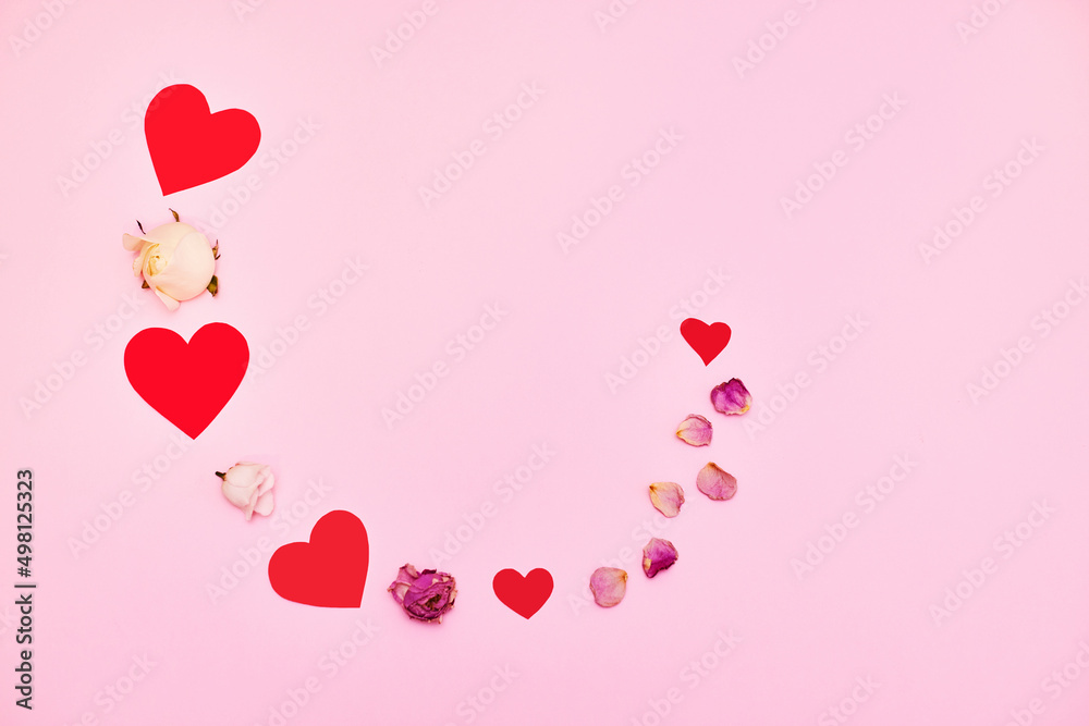 red paper hearts and rose petals on pink background.