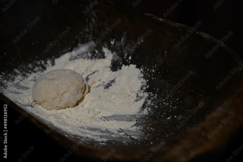 The cooking process of a bread dough. Baking bread recipe. Bakery breads food, detail view with woman hands working on dough at an old wood pan. flour falling on a dark table. detail. The cooking process of a bread dough. Baking bread recipe. Bakery breads food, detail view with woman hands working on dough at an old wood pan. flour falling on a dark table. detail.